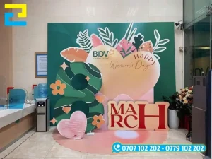 Mẫu 20: Backdrop 8/3 được trang trí viền hoa đẹp bắt mắt, có kiểu chữ đơn giản - nghệ thuật, phông nền có tông màu xanh chủ đạo